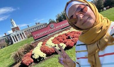 Buthina stands in front of a red BSU sign with Boyden Hall in the background.